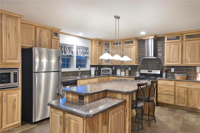 kitchen with a sink, wall chimney range hood, appliances with stainless steel finishes, a center island, and dark countertops