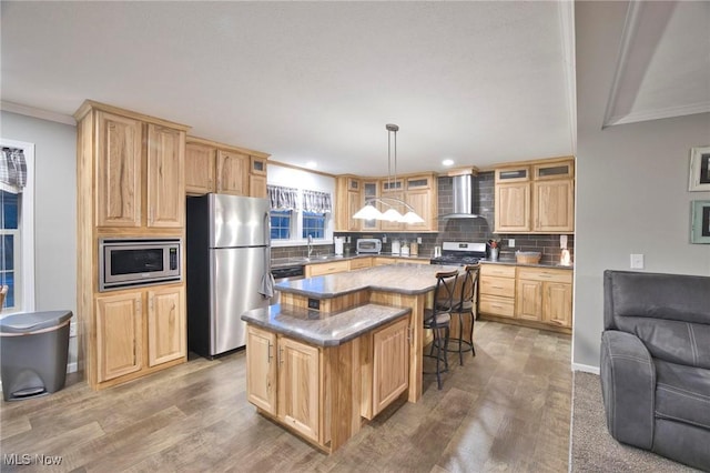 kitchen with wall chimney exhaust hood, tasteful backsplash, light brown cabinetry, appliances with stainless steel finishes, and a kitchen breakfast bar