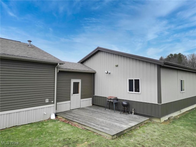 rear view of house featuring a deck, a yard, and a shingled roof