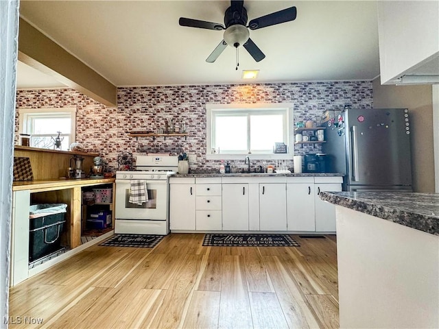 kitchen featuring a wealth of natural light, freestanding refrigerator, white cabinetry, and white gas range oven