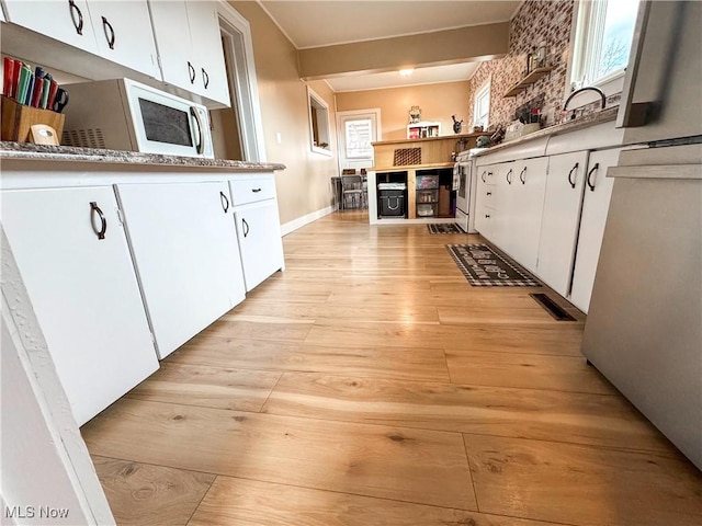 kitchen featuring light wood finished floors, visible vents, white cabinets, white microwave, and light countertops