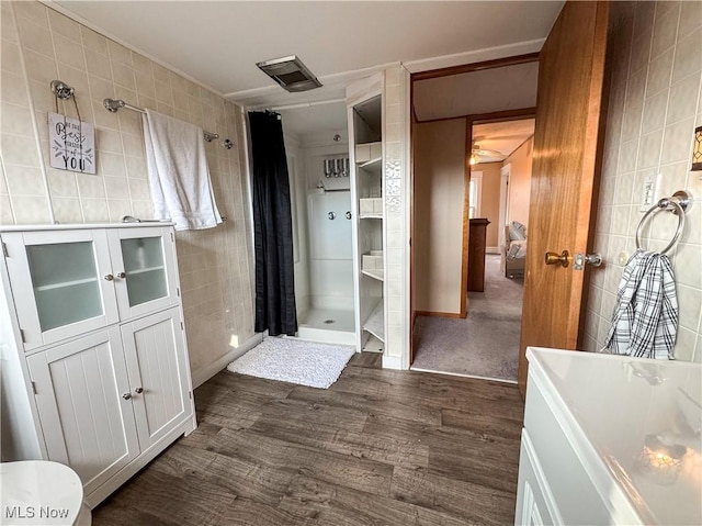 bathroom with a tile shower, tile walls, and wood finished floors