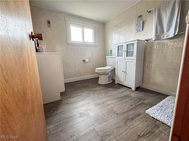 bathroom with toilet, wood finished floors, tile walls, and baseboards