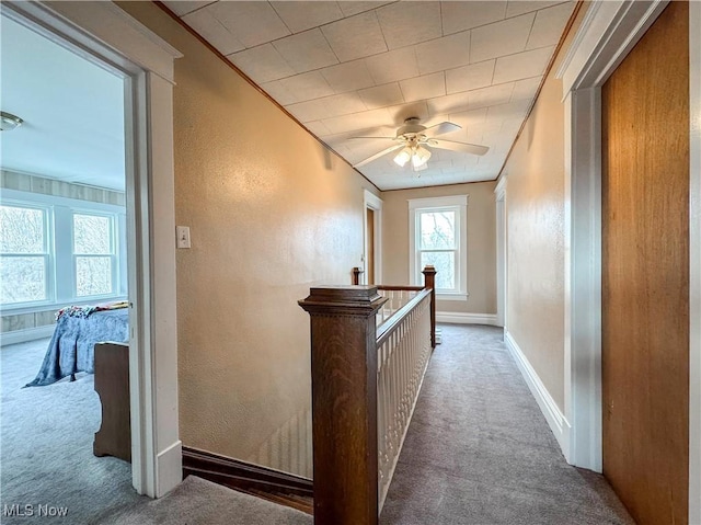 hallway featuring a textured wall, carpet floors, an upstairs landing, and baseboards