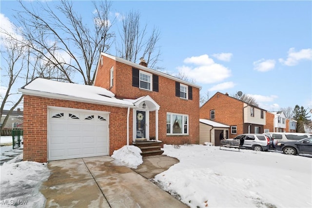 colonial home with an attached garage, a chimney, concrete driveway, and brick siding