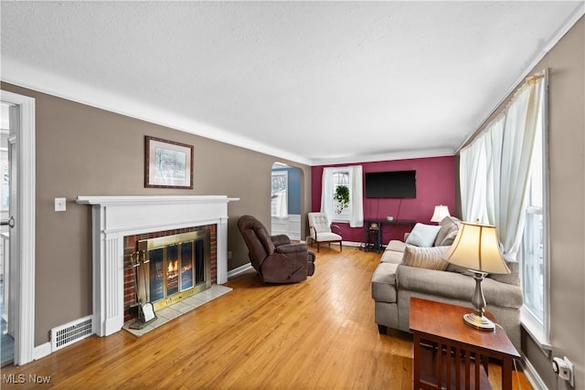 living area featuring a brick fireplace, baseboards, visible vents, and wood finished floors