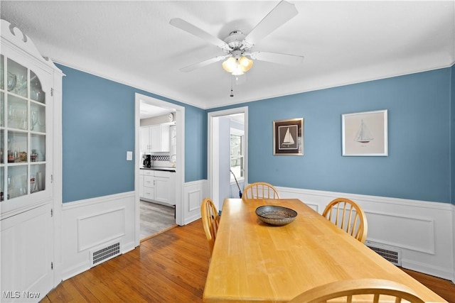 dining area with wainscoting, visible vents, ceiling fan, and wood finished floors