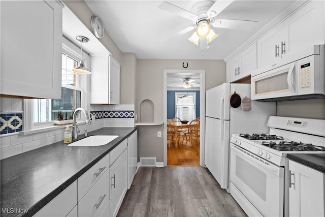 kitchen featuring white appliances, plenty of natural light, visible vents, dark countertops, and a sink