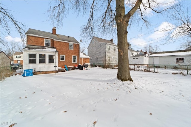 snow covered house with brick siding, fence, and a chimney