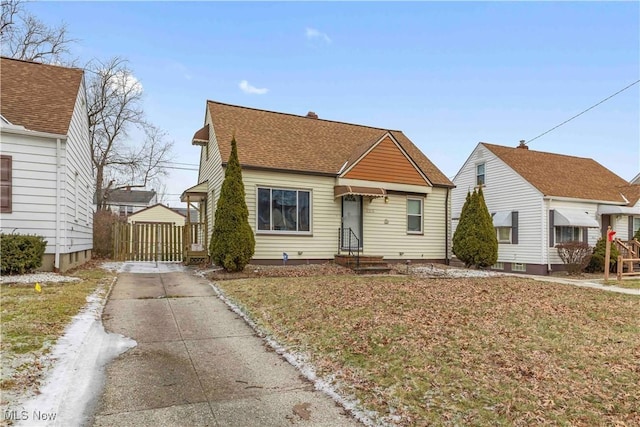 bungalow-style home featuring a gate, a front lawn, concrete driveway, and roof with shingles