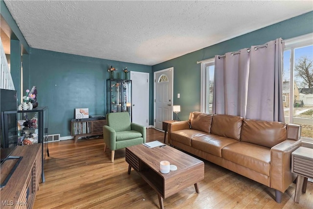 living room featuring visible vents, a textured ceiling, baseboards, and wood finished floors