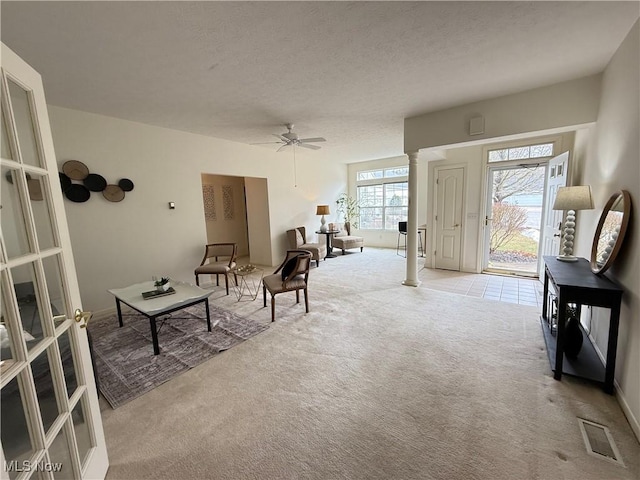 interior space featuring visible vents, a ceiling fan, light carpet, a textured ceiling, and ornate columns