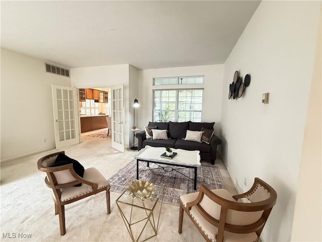 living area featuring a wealth of natural light, french doors, visible vents, and light colored carpet