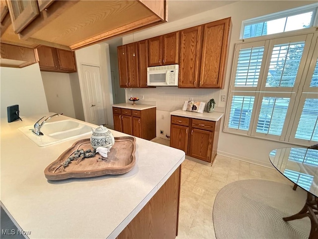 kitchen with light countertops, white microwave, a sink, and brown cabinets