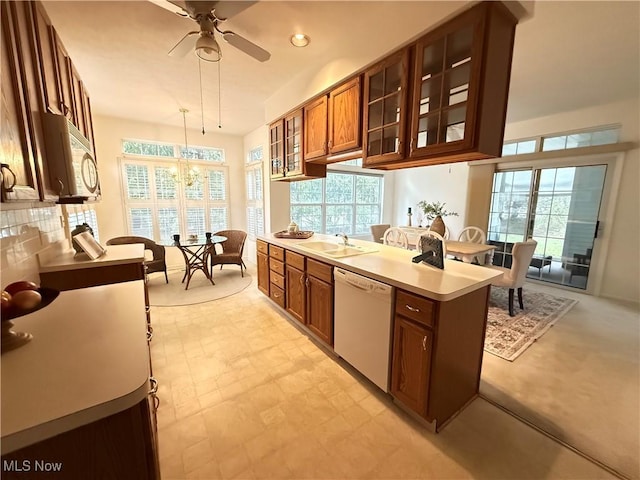 kitchen featuring white appliances, a sink, light countertops, brown cabinets, and glass insert cabinets