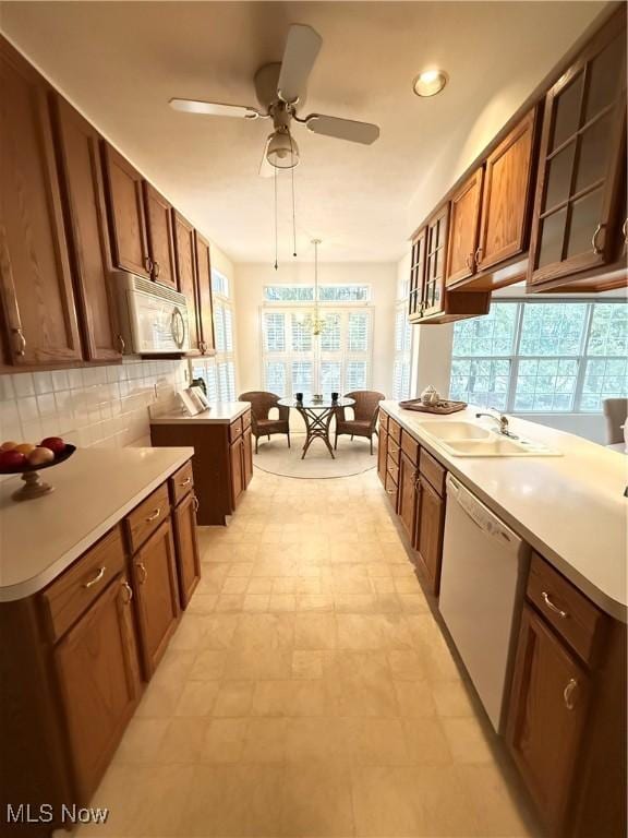 kitchen featuring backsplash, glass insert cabinets, brown cabinetry, a sink, and white appliances