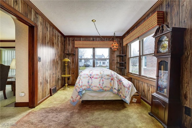 bedroom featuring a textured ceiling, arched walkways, wooden walls, carpet floors, and visible vents