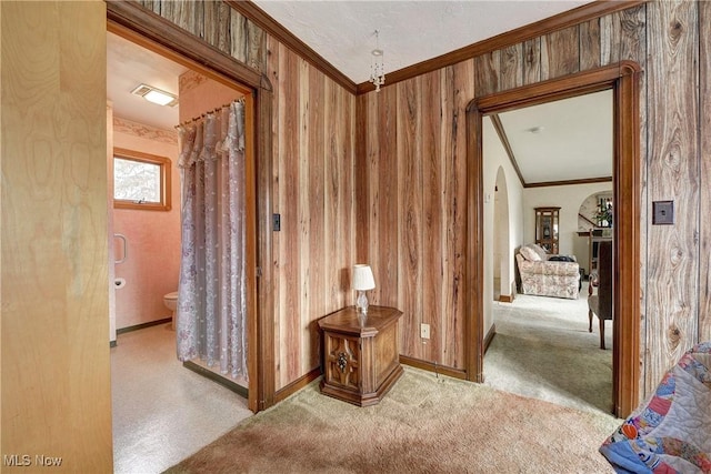 corridor featuring arched walkways, carpet floors, wood walls, visible vents, and crown molding