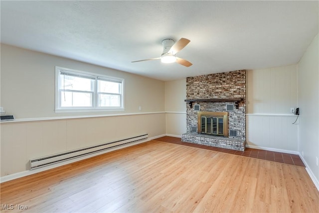 unfurnished living room featuring a baseboard heating unit, a brick fireplace, ceiling fan, and wood finished floors