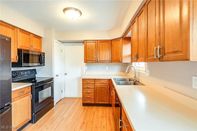 kitchen featuring stainless steel appliances, a sink, light wood-style floors, light countertops, and brown cabinetry