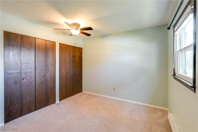 unfurnished bedroom with multiple closets, carpet flooring, ceiling fan, and baseboards