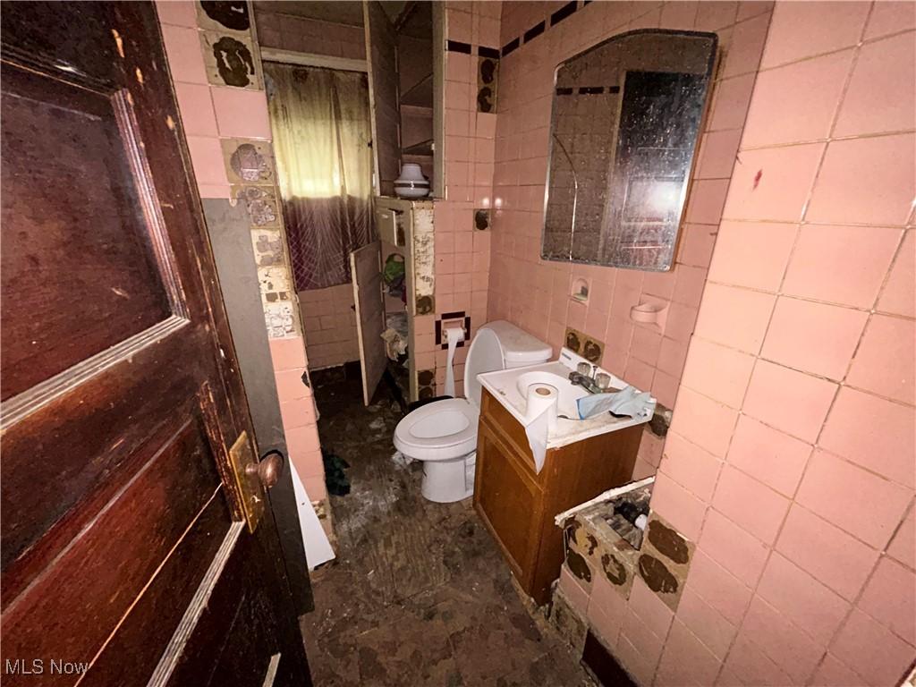 bathroom featuring toilet, tile walls, and vanity