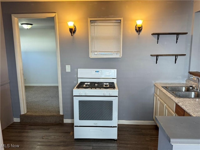 kitchen featuring dark wood finished floors, gas range gas stove, open shelves, a sink, and baseboards