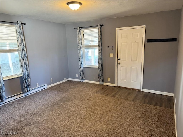 unfurnished room featuring baseboard heating, baseboards, and dark colored carpet