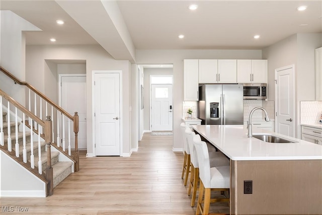 kitchen with light wood-type flooring, backsplash, stainless steel appliances, and a sink