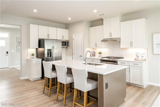 kitchen with a center island with sink, stainless steel appliances, under cabinet range hood, a kitchen bar, and a sink