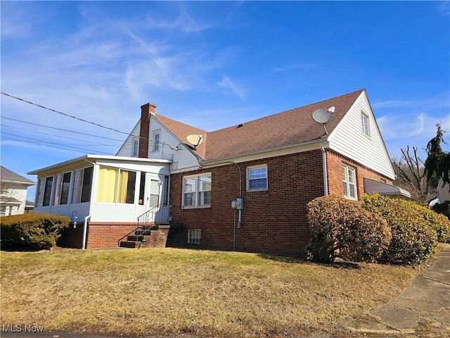 exterior space with a sunroom, brick siding, a yard, and a chimney