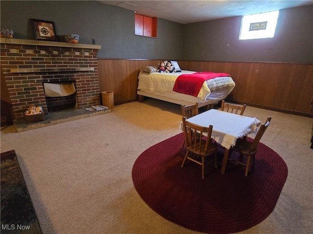 bedroom with carpet floors, a wainscoted wall, wooden walls, and a brick fireplace