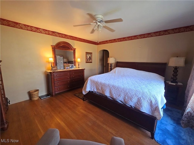 bedroom with a ceiling fan, arched walkways, baseboards, and wood finished floors