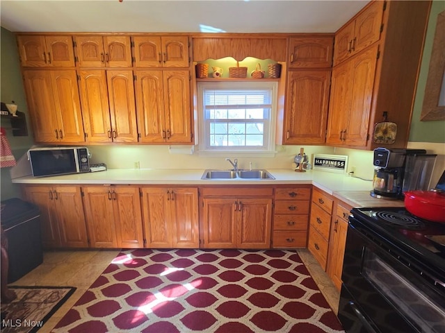 kitchen featuring black electric range, brown cabinetry, light countertops, and a sink