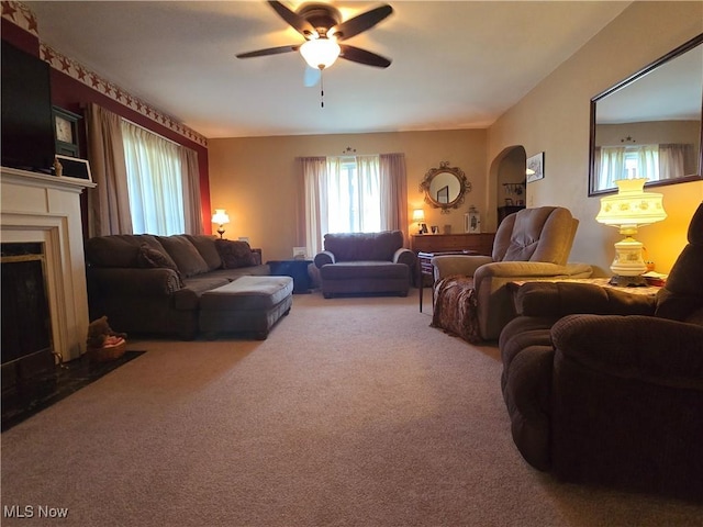 living area with carpet floors, ceiling fan, and a fireplace with flush hearth