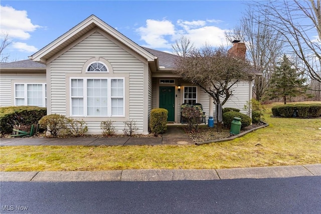 ranch-style house with a shingled roof, a chimney, and a front yard