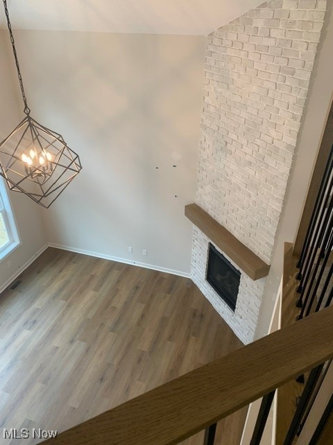 unfurnished living room with a notable chandelier, visible vents, a large fireplace, wood finished floors, and baseboards