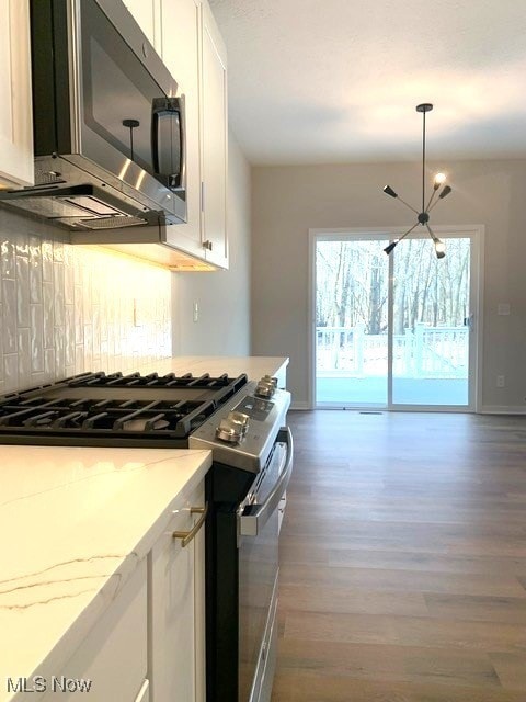 kitchen with light stone countertops, decorative backsplash, appliances with stainless steel finishes, white cabinets, and wood finished floors