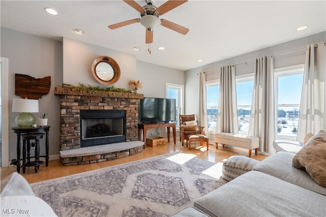 living room with baseboards, ceiling fan, wood finished floors, a stone fireplace, and recessed lighting