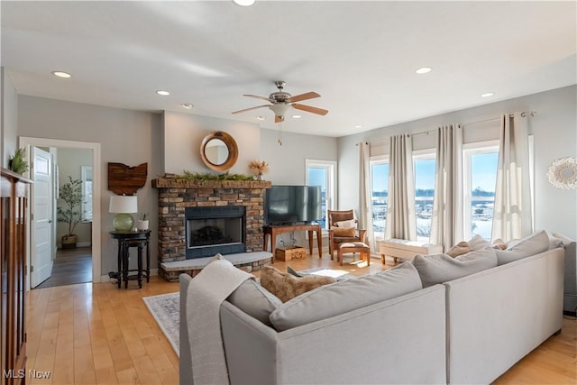 living room featuring a fireplace with raised hearth, a ceiling fan, light wood-style flooring, and recessed lighting