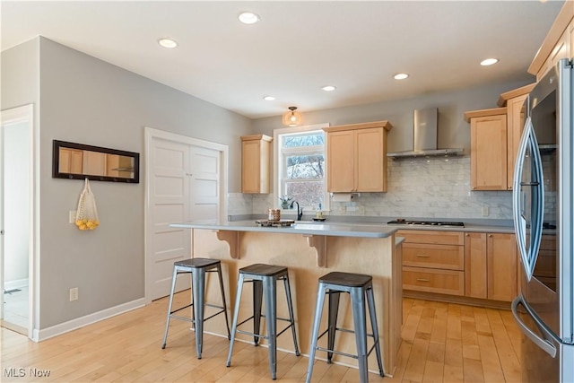 kitchen with stainless steel appliances, light countertops, light wood-style flooring, light brown cabinets, and wall chimney exhaust hood