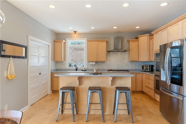 kitchen with wall chimney exhaust hood, appliances with stainless steel finishes, a breakfast bar area, light countertops, and light brown cabinetry