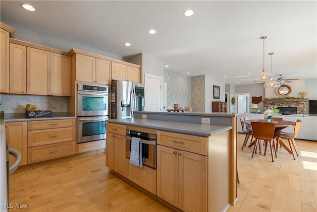 kitchen with stainless steel appliances, light brown cabinets, backsplash, and light wood finished floors