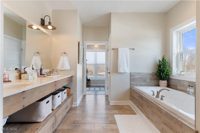 bathroom featuring wood finished floors, a sink, baseboards, and a bath