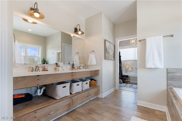 full bathroom with a relaxing tiled tub, a healthy amount of sunlight, baseboards, and wood finished floors