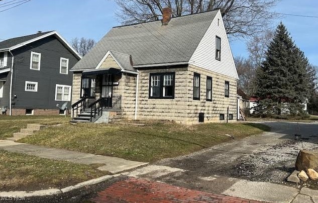 view of front of property featuring a front yard, roof with shingles, and a chimney