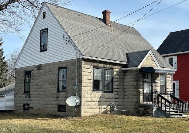 view of front facade featuring a front yard, roof with shingles, and a chimney