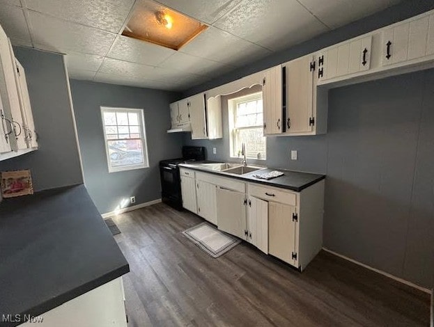 kitchen with dark countertops, black gas range, dark wood-type flooring, a sink, and baseboards