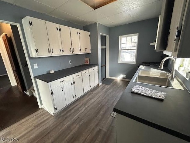 kitchen with dark countertops, white cabinets, dark wood-style flooring, and a sink