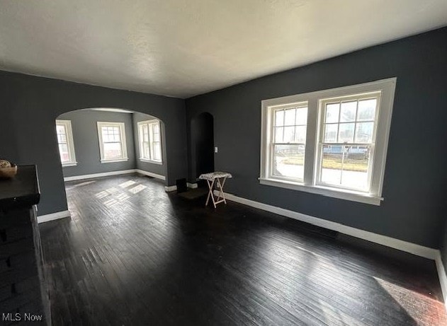 interior space featuring arched walkways, dark wood finished floors, and baseboards